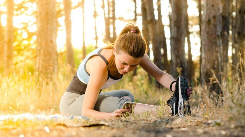 Woman stretching in forest, sunlight filtering through trees.