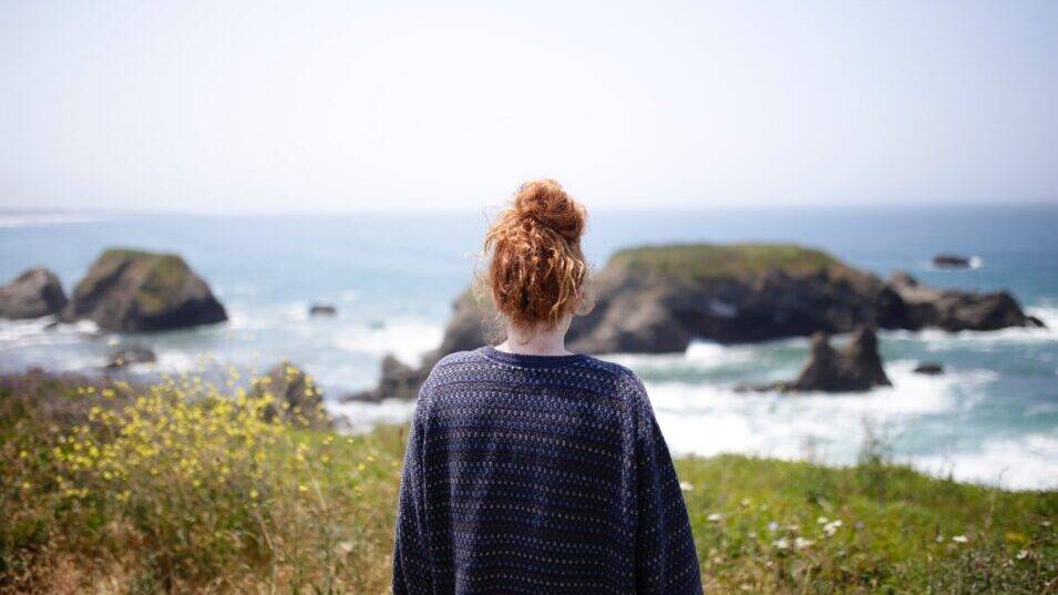 Woman admiring scenic coastal view with rocky ocean cliffs.