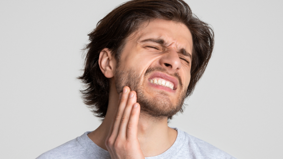 Man with toothache holding jaw, expressing pain.