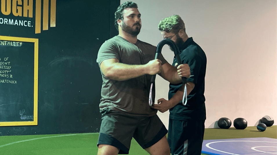 Two men exercising with a resistance band in a gym setting.